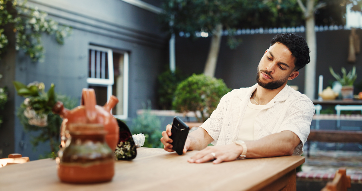 En mann som sitter ved et bord og ser tomt inn i mobilen sin